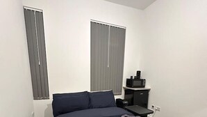 Un dormitorio con cama, mesita de noche, televisor y dos ventanas con persianas.