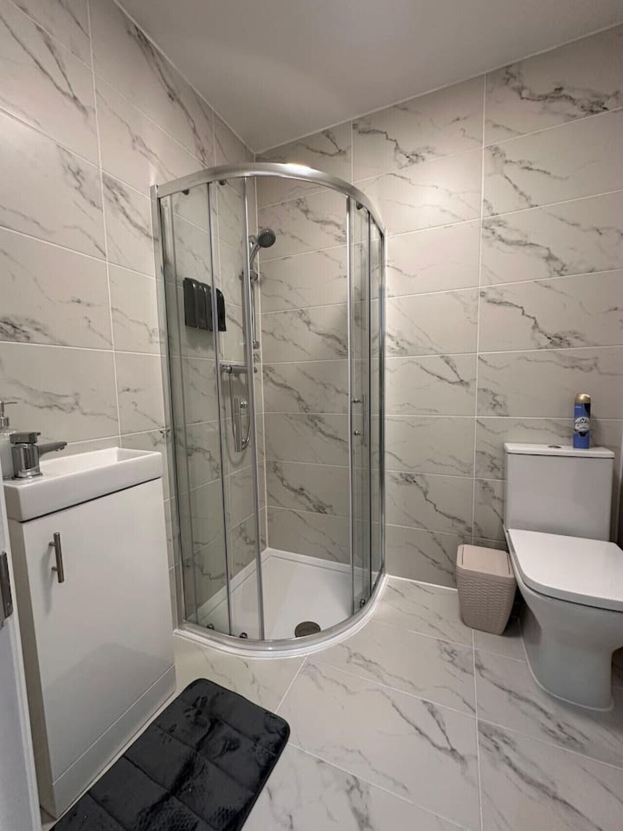 A modern bathroom with a glass-enclosed shower, a white sink, and a toilet.