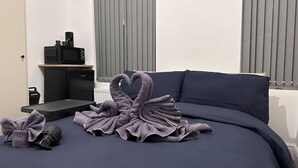 Ein ordentlich bezogenes Bett mit einer schwanenförmigen Handtuch-Arrangement, ein kleiner Tisch mit Kaffeemaschine und ein Heizkörper im Hintergrund.