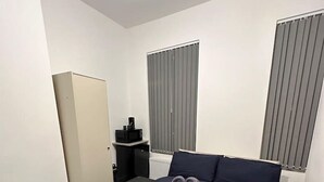 Ein Hotelzimmer mit Bett, Kleiderschrank, einem kleinen Tisch mit Wasserkocher und einem Fenster mit Jalousien.