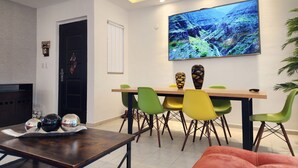 Un espace repas moderne avec une table en bois et des chaises colorées, un téléviseur à écran plat fixé au mur et un vase décoratif.