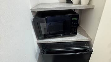 A compact kitchenette with a microwave, a small refrigerator, and a shelf with cups and a coffee maker.