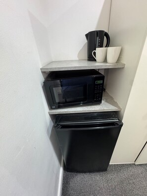 A compact kitchenette with a microwave, a small refrigerator, and a shelf with cups and a coffee maker. - London Victoria 15 minutes away (Greater London)