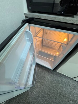 Een open koelkast met een vriesvak en een magnetron erboven.