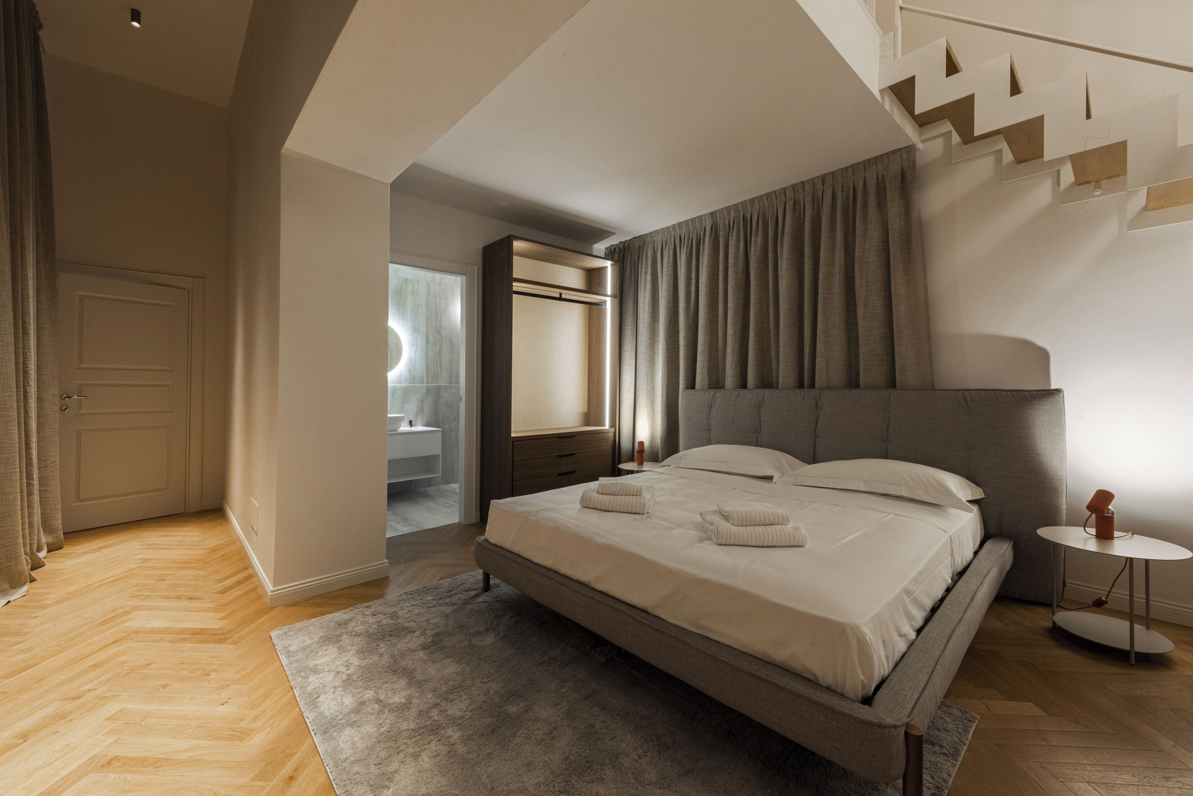 A modern bedroom with a large bed, a bedside table, and a view of a bathroom.