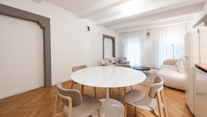 Una sala de estar moderna con una mesa redonda blanca rodeada por cuatro sillas, un sofá y un espejo grande en la pared.