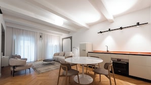 Una cocina moderna con armarios blancos, horno empotrado y encimera. Hay un comedor con una mesa redonda y cuatro sillas.