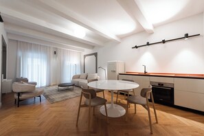 Eine moderne Küche mit weißen Schränken, einem eingebauten Backofen und einer Arbeitsplatte. Es gibt eine Essecke mit einem runden Tisch und vier Stühlen.