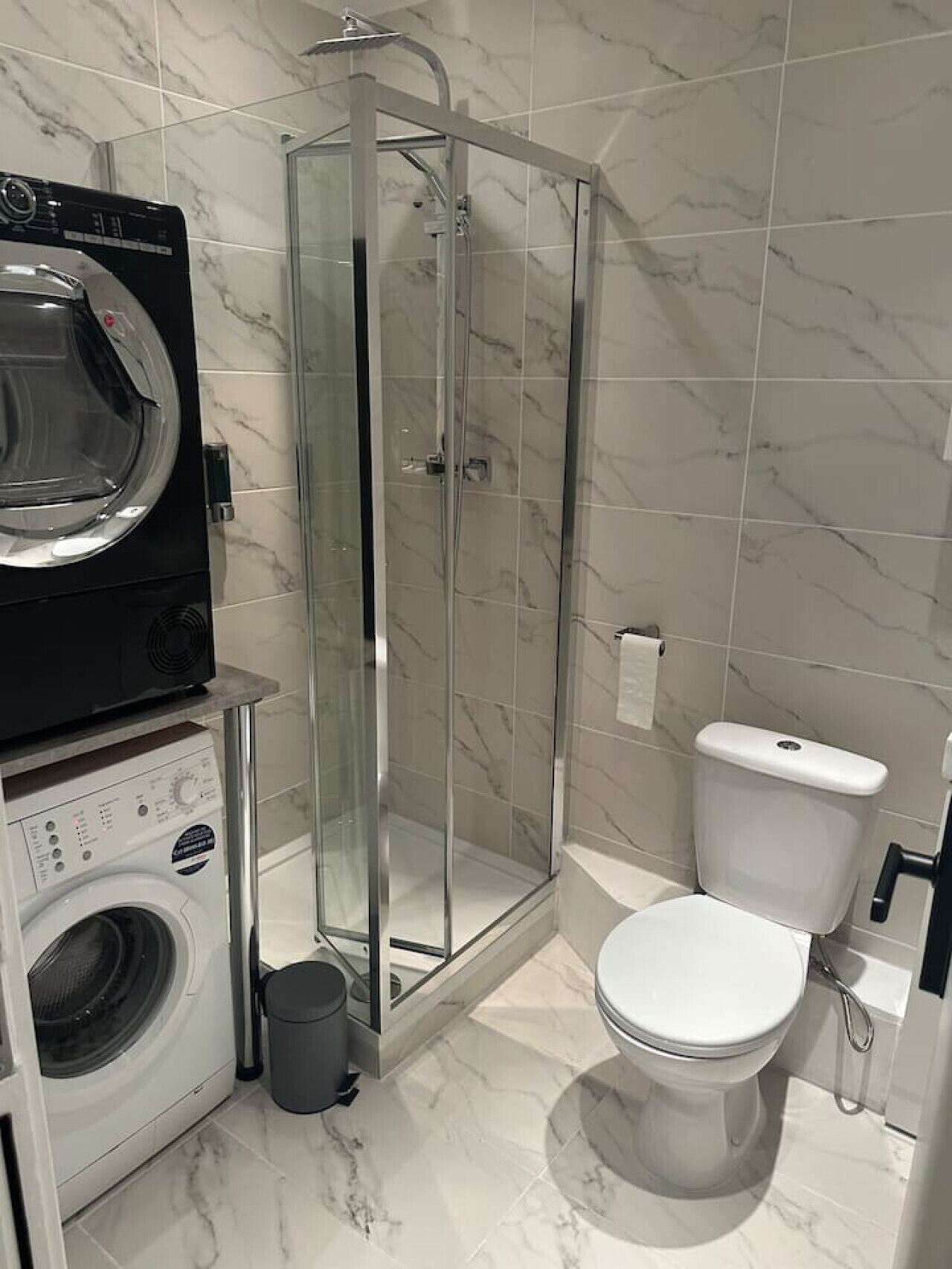 A compact bathroom with a washing machine, a glass-enclosed shower, and a toilet.