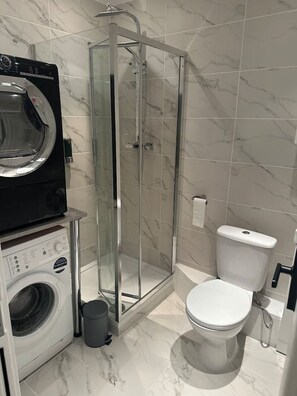 Un baño pequeño con lavadora, ducha con mampara de vidrio e inodoro.