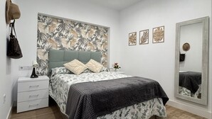 A bedroom with a bed, a nightstand, a mirror, and a wall with a tropical leaf pattern. - Secunda Romana (Cordoba)