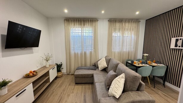 A modern living room with a sofa, a TV, a dining area with chairs and a table, and a kitchen counter with a plant. - Secunda Romana (Cordoba)
