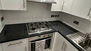A compact kitchen with white cabinets, a stainless steel range hood, a gas stove, a built-in oven, and a sink. - London Waterloo Moments away (Greater London)