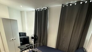 A compact hotel room with a bed, a desk, a chair, a wardrobe, and a small kitchenette. - London Waterloo Moments away (Greater London)