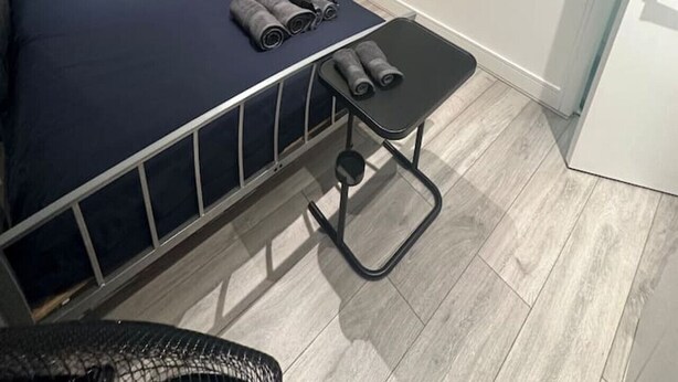 A bedroom with a bed, a small table with rolled-up towels, a mirror, and a door leading to another room. - London Waterloo Moments away (Greater London)
