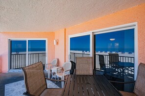 En balkon med udsigt over stranden, møbleret med fletstole og et bord.