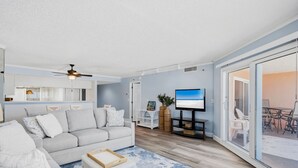 Ein modernes Wohnzimmer mit einem grauen Sofa, einem Flachbildfernseher und einer Schiebetür zu einem Außenbereich.