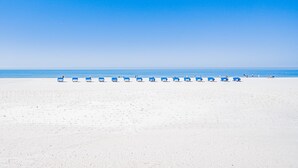 Ein Strand mit Reihen aus blauen Liegestühlen und Sonnenschirmen.