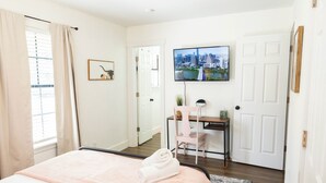 Habitación de hotel con cama, escritorio, silla, televisor y puerta.
