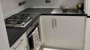 Cocina compacta con armarios blancos, estufa a gas, lavamanos y salpicadero de azulejos.