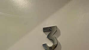 Placa metálica con el número 3 en una pared.
