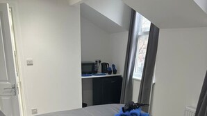 Ett modernt sovrum med en säng, ett litet skrivbord, en spegel och en liten köksdel.