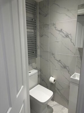 A bathroom with a toilet, marble walls, and a shower area. - London Eye/Big Ben 10 mins away (Greater London)