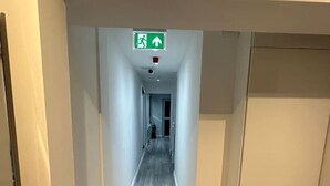 A narrow hallway with a wooden floor and white walls, leading to a door at the end. - Central London- Zone 1/2 En-suite Room (Greater London)