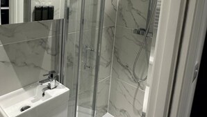 A modern bathroom with a glass-enclosed shower, white marble tiles, and a visible sink area. - London Bridge 15 minutes away (Greater London)