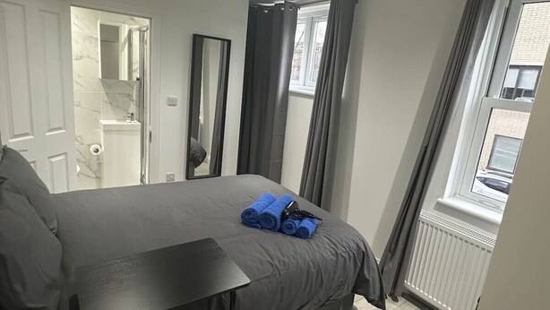 A bedroom with a bed, a bedside table, a mirror, and a window with curtains. - London Bridge 15 minutes away (Greater London)