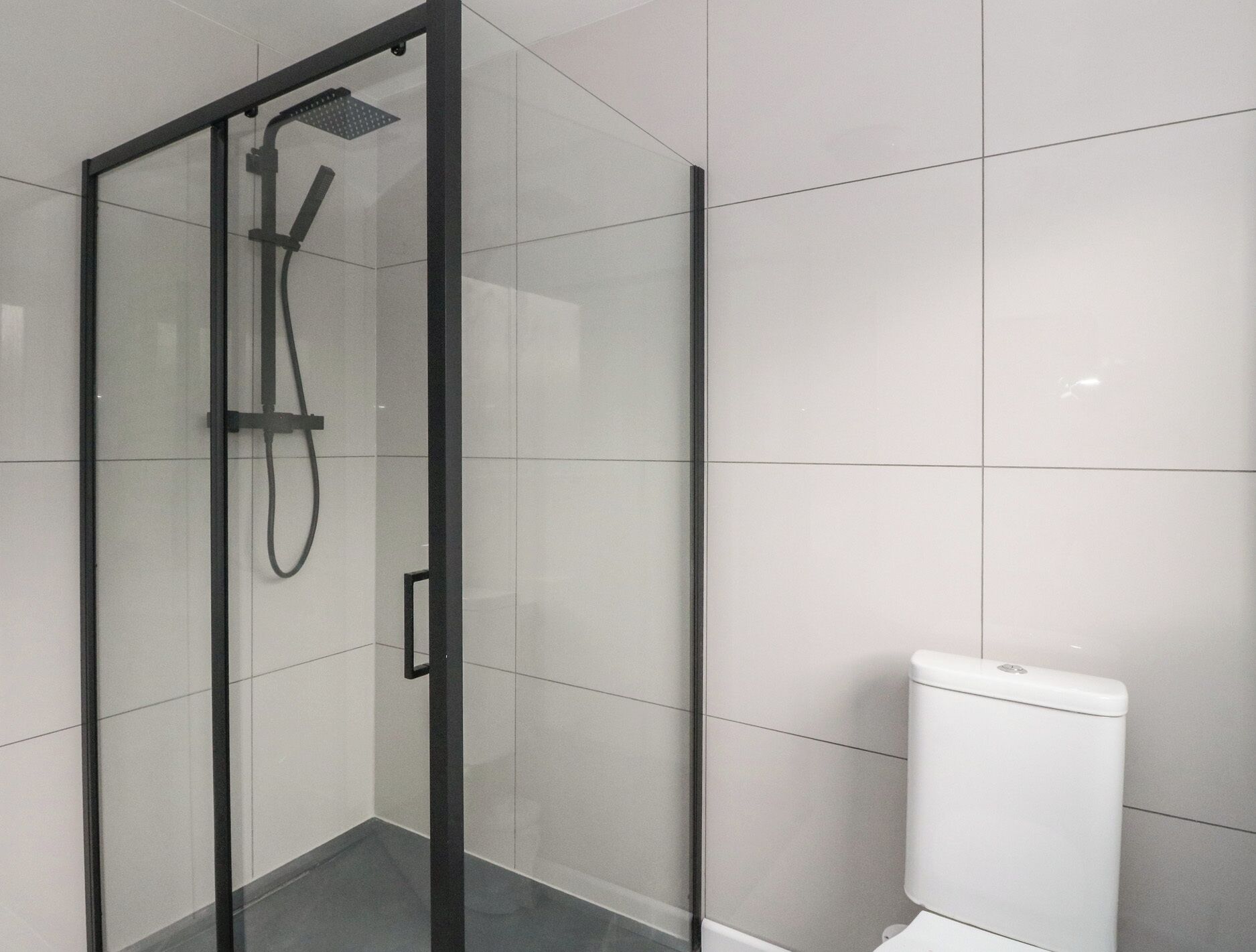 A modern bathroom with a glass-enclosed shower, white tiled walls, and a white toilet.