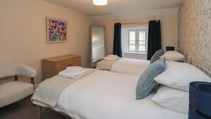 Une chambre à coucher avec un lit, une chaise, une commode, un miroir et une fenêtre avec des rideaux.