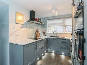 Une cuisine moderne avec des meubles gris, un plan de travail en marbre, un four encastré et une fenêtre donnant sur l’extérieur.