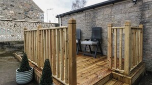 Une terrasse en bois avec un muret en pierre, deux plantes en pot et deux chaises.