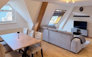 Ein modernes Loft-Apartment mit Essbereich, Sofa, Fernseher und Dachfenster.