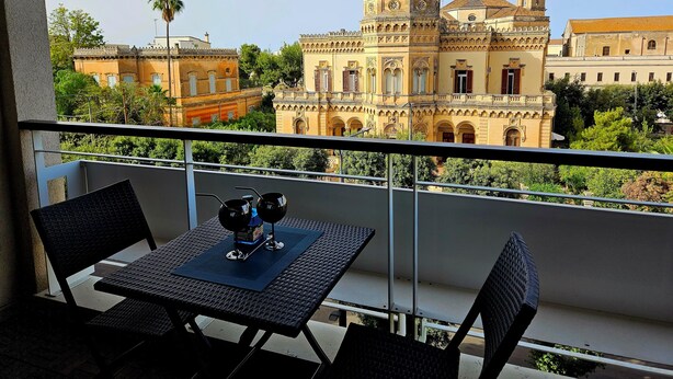 A balcony with a table and chairs, overlooking a historic building with ornate architecture.