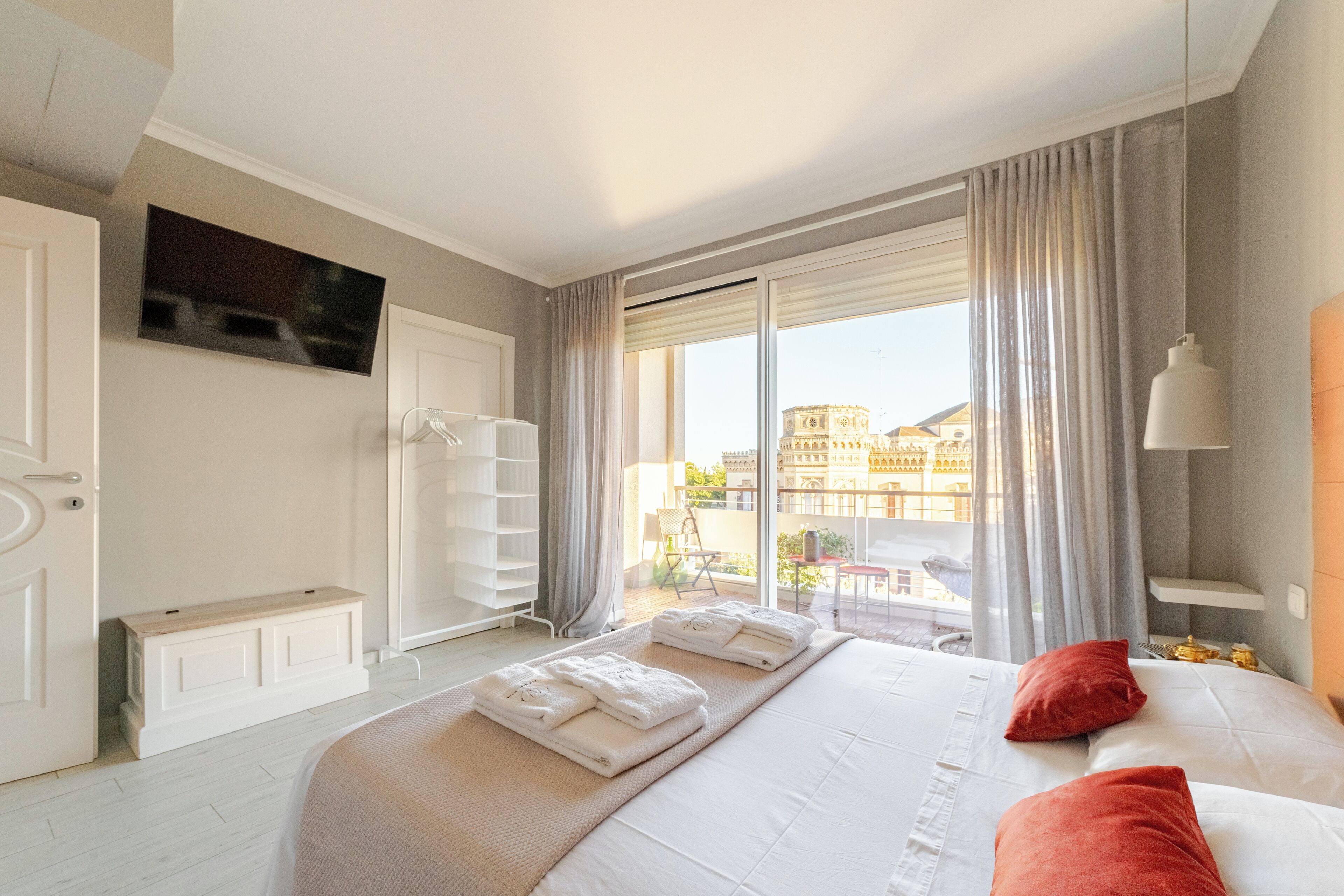 Une chambre d’hôtel avec un grand lit, une vue sur un immeuble par la fenêtre et un téléviseur fixé au mur.