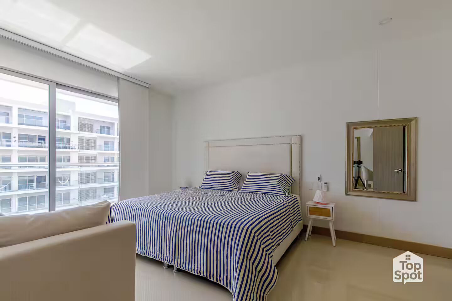 Ein modernes Hotelzimmer mit einem großen Bett, einem Nachttisch, einem Spiegel und einem Fenster mit Blick auf die Stadt.
