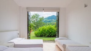 Quarto com duas camas e uma grande porta de correr de vidro que dá para um jardim com vegetação e vista para a montanha.