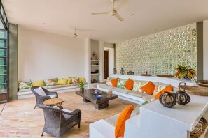 Un salon spacieux avec un canapé blanc, des fauteuils en osier, une table basse et un mur décoratif.