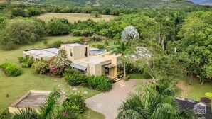 Uma casa moderna com telhado plano, cercada por vegetação exuberante e colinas ao fundo.