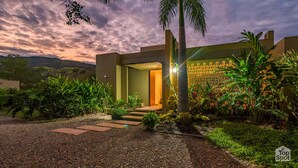 Um edifício moderno com um jardim bem cuidado, entrada pavimentada e vista para a paisagem circundante.