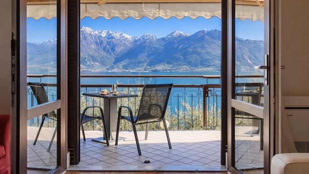 A balcony with a table and chairs, a view of mountains, and a lake. - Mont&Lac | Lake View Apartment in Limone (Limone Sul Garda)