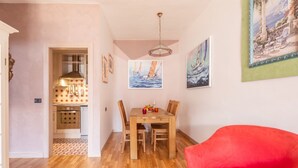 A dining area with a wooden table and chairs, a red sofa, and artwork on the walls. - Mont&Lac | Lake View Apartment in Limone (Limone Sul Garda)