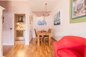 A dining area with a wooden table and chairs, a red sofa, and artwork on the walls. - Mont&Lac | Lake View Apartment in Limone (Limone Sul Garda)