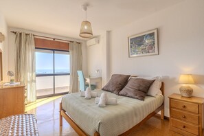 Un dormitorio con cama, mesita de noche y vistas al mar a través de un ventanal grande.
