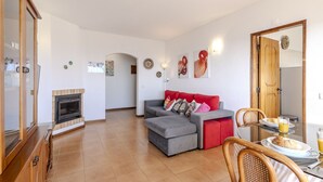 Ein Wohnzimmer mit Kamin, einem roten Sofa, einem Esstisch mit Tellern und Gläsern sowie einem Holzschrank.