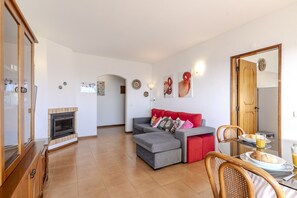 Una sala de estar con chimenea, un sofá rojo, una mesa de comedor con platos y vasos, y un aparador de madera.