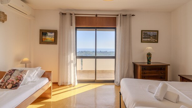 Ein Hotelzimmer mit einer großen Schiebeglastür zum Balkon, einem Bett mit weißer Bettwäsche, einem Nachttisch mit Lampe und zwei gerahmten Bildern an den Wänden.