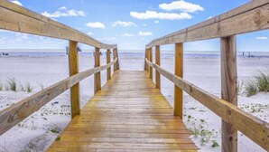 Ein hölzerner Steg führt zu einem Strand unter blauem Himmel.